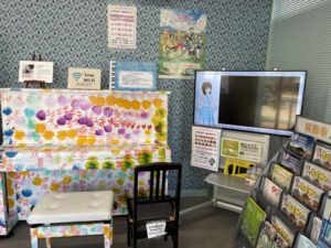 （コラボに関係はない）アップライトピアノとその隣のディスプレイ。ディスプレイにはアイマスチャンネルが映されている。